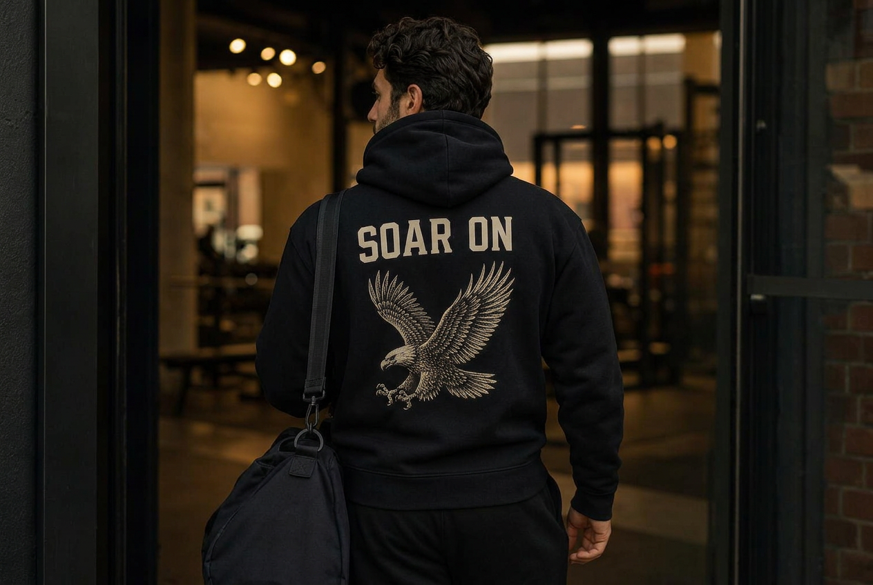 Man walking into the gym wearing the black SOAR ON heavyweight hoodie, cream eagle back print in focus